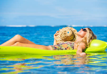 Beautiful young woman floating on raft in tropical ocean