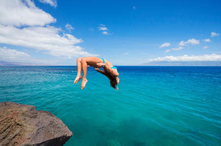 Woman doing backflip off cliff into the ocean. Summer fun lifestyle.の写真素材