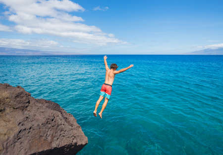 Man jumping off cliff into the ocean. Summer fun lifestyle.の写真素材