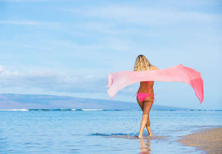 Beautiful woman walking on tropical beach with sarong blowing in the windの写真素材