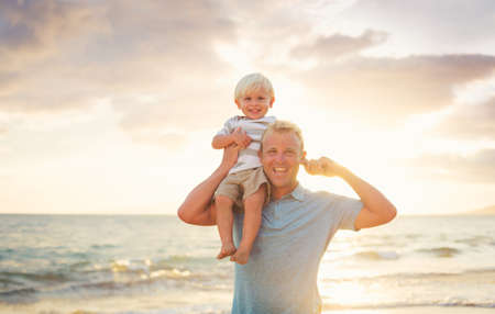 Father holding son on his shoulders on the beach at sunset. 