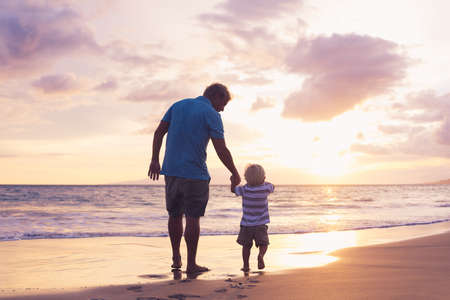 Father and son holding hands walking on the beach at sunsetの写真素材