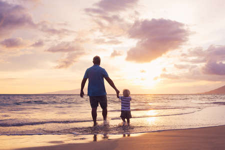 Father and son holding hands walking on the beach at sunset