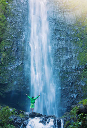 Man standing at the base of large waterfall in Hawaiiの写真素材