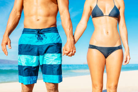Attractive Fit Couple on the Beach in Swimwear Holding Handsの写真素材