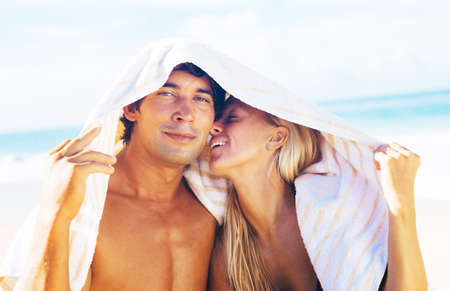Portrait of Attractive Happy Couple on the Beach. Hiding from the Sun and Sharing Intimate Moment Under Beach Towel.の写真素材