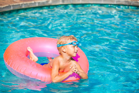 Young Kid Having Fun in the Swimming Pool On Inner Tube Raft. Summer Vacation Fun.