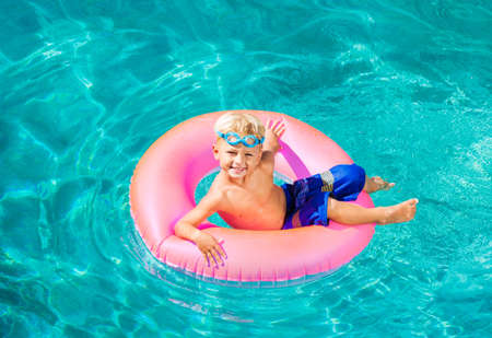Young Kid Having Fun in the Swimming Pool On Inner Tube Raft. Summer Vacation Fun.