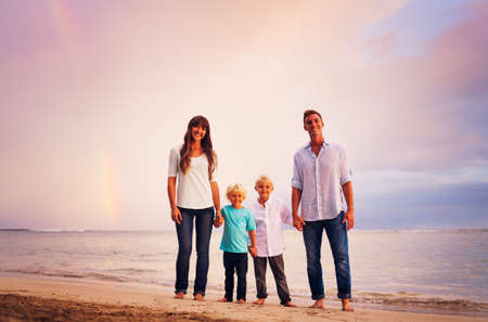 Happy young family on the beach at sunset with amazing rainbow