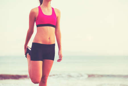 Healthy Active Lifestyle. Young fitness woman stretching and preparing for workout on the beach at sunset.の写真素材