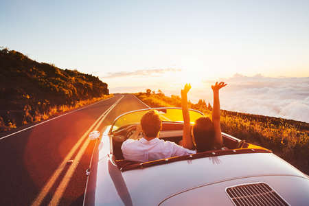 Happy Couple Driving on Country Road into the Sunset in Classic Vintage Sports Carの写真素材