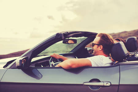 Happy Young Couple Driving Along Country Road in Convertible at Sunsetの写真素材