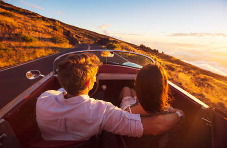 Driving into the Sunset. Romantic Young Couple Enjoying Sunset Drive in Classic Vintage Sports Carの写真素材