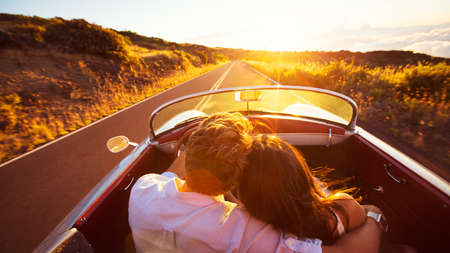 Driving into the Sunset. Romantic Young Couple Enjoying Sunset Drive in Classic Vintage Sports Carの写真素材