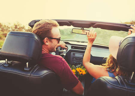 Happy Young Couple Driving Along Country Road in Convertible at Sunsetの写真素材