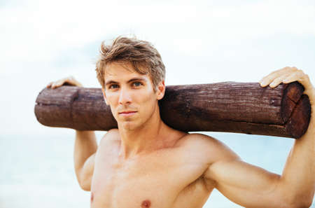 CrossFit beach workout. Male athlete exercising outdoors at the beach with tree log. Fitness and healthy lifestyle.の写真素材