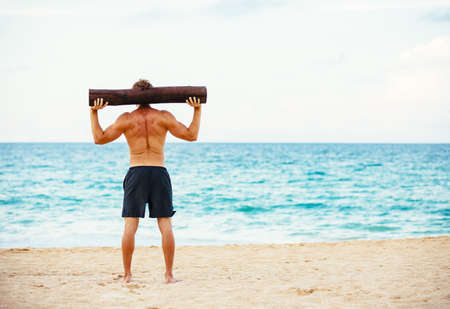 CrossFit beach workout. Male athlete exercising outdoors at the beach with tree log. Fitness and healthy lifestyle.の写真素材
