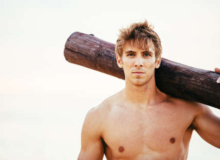 CrossFit beach workout. Male athlete exercising outdoors at the beach with tree log. Fitness and healthy lifestyle.の写真素材