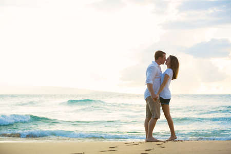 Romantic Happy Young Couple Kissing on the Beach at Sunsetの写真素材