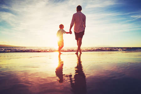 Father and Son Holding Hands Walking Together on the Beach at Sunsetの写真素材