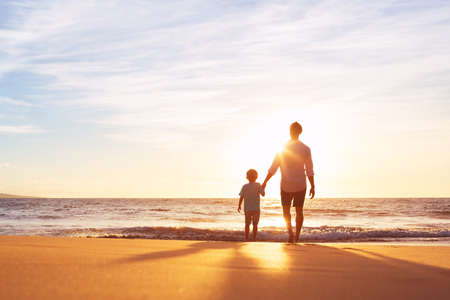 Father and Son Holding Hands Walking Together on the Beach at Sunsetの写真素材