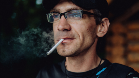 A man smokes a cigarette. Guy with glasses smokes cigarettes. Tobacco smokeの写真素材