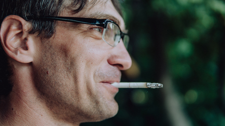 A man smokes a cigarette. Guy with glasses smokes cigarettes. Tobacco smokeの写真素材