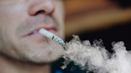 A man smokes a cigarette. Guy with glasses smokes cigarettes. Tobacco smokeの写真素材