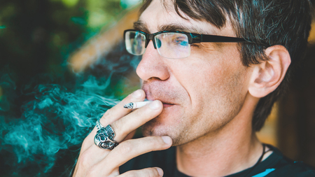 A man smokes a cigarette. Guy with glasses smokes cigarettes. Tobacco smokeの写真素材