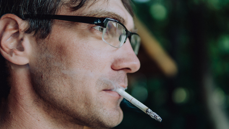 A man smokes a cigarette. Guy with glasses smokes cigarettes. Tobacco smokeの写真素材