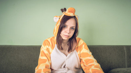 girl in a bright children's pajamas in the form of a kangaroo. emotional portrait of a student. costume presentation of children's animator. Slippers in the form of cat's paws.の写真素材