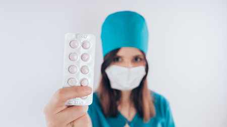 beautiful young woman with a bandage on her face, isolated on white background. Female doctor in medical gown holds pills. Healthcare personnel, medicine conceptの写真素材
