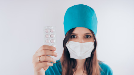 beautiful young woman with a bandage on her face, isolated on white background. Female doctor in medical gown holds pills. Healthcare personnel, medicine conceptの写真素材