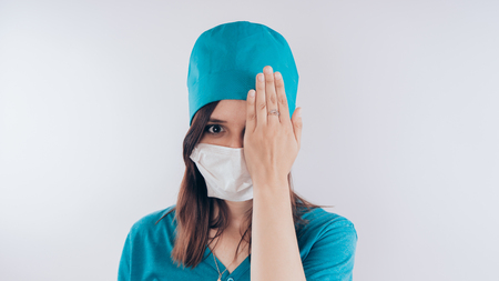 Portrait of a friendly smiling doctor. Hand closed one eye, the concept of "vision check", isolated on white background with copy space. Healthcare and medicineの写真素材