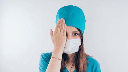Portrait of a friendly smiling doctor. Hand closed one eye, the concept of "vision check", isolated on white background with copy space. Healthcare and medicineの写真素材