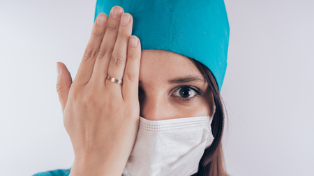 Portrait of a friendly smiling doctor. Hand closed one eye, the concept of "vision check", isolated on white background with copy space. Healthcare and medicineの写真素材
