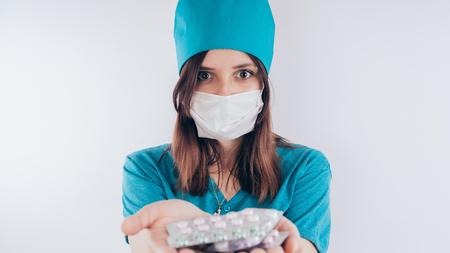 beautiful young woman with a bandage on her face, isolated on white background. Female doctor in medical gown holds pills. Healthcare personnel, medicine conceptの写真素材