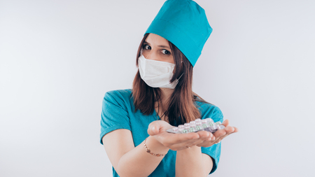 beautiful young woman with a bandage on her face, isolated on white background. Female doctor in medical gown holds pills. Healthcare personnel, medicine conceptの写真素材