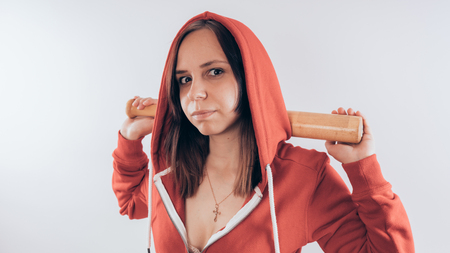 Girl athlete with a baseball bat in a red hoodie. Girl or criminal woman holding baseball bat in hand on white background. Body art. Sport and trainingの写真素材