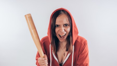 Girl athlete with a baseball bat in a red hoodie. Girl or criminal woman holding baseball bat in hand on white background. Body art. Sport and trainingの写真素材