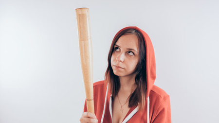 Girl athlete with a baseball bat in a red hoodie. Girl or criminal woman holding baseball bat in hand on white background. Body art. Sport and trainingの写真素材