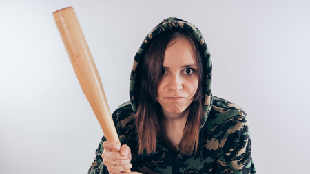 Girl with a bat in a sweatshirt in the colors of camouflage. Girl or criminal woman holding baseball bat in hand on white background. Body art. Sport and trainingの写真素材