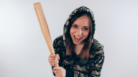 Girl with a bat in a sweatshirt in the colors of camouflage. Girl or criminal woman holding baseball bat in hand on white background. Body art. Sport and trainingの写真素材