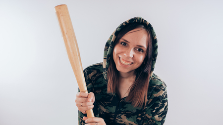 Girl with a bat in a sweatshirt in the colors of camouflage. Girl or criminal woman holding baseball bat in hand on white background. Body art. Sport and trainingの写真素材