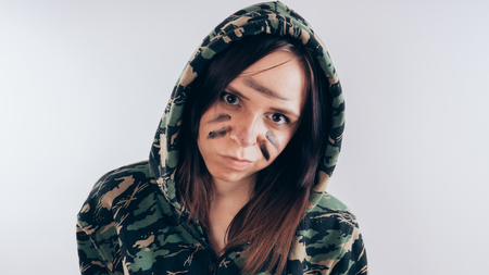 Girl with a bat in a sweatshirt in the colors of camouflage. Girl or criminal woman holding baseball bat in hand on white background. Body art. Sport and trainingの写真素材