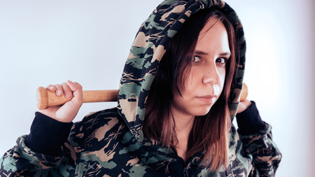 Girl with a bat in a sweatshirt in the colors of camouflage. Girl or criminal woman holding baseball bat in hand on white background. Body art. Sport and trainingの写真素材