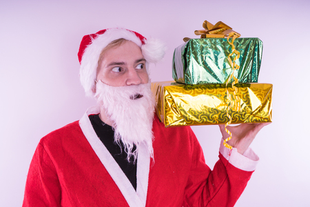 Portrait of thin Santa Claus with Christmas gifts. Happy Santa Claus holding gift boxes isolated on white background. Santa Claus carries gifts to children.の写真素材