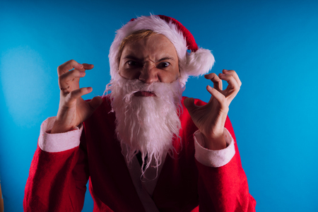 Emotional Santa Claus on a blue background. The concept of bad Santa Claus. Happy New Year and merry Christmas!の写真素材