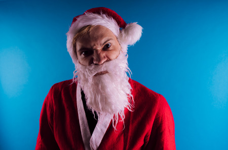 Emotional Santa Claus on a blue background. The concept of bad Santa Claus. Happy New Year and merry Christmas!の写真素材