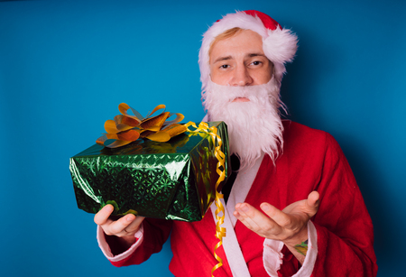 Portrait of thin Santa Claus with Christmas gifts. Happy Santa Claus is holding gift boxes isolated on blue background. Santa Claus carries gifts to children.の写真素材